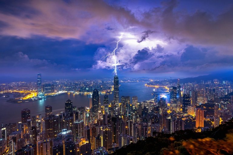 Güneş – Neptün & Plüton Etkisi: Gerçek ve Dönüşümün Çarpışması Gece vakti şimşekler ve aydınlatılmış gökdelenlerle Hong Kong şehir manzarası
